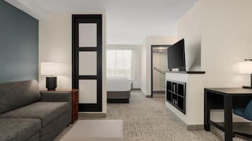 A hotel room with a sofa, a bed, a desk, a television, and a bathroom visible through an open door.