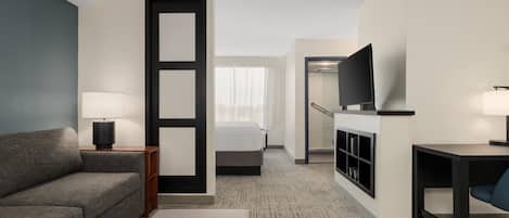 A hotel room with a sofa, a bed, a desk, a television, and a bathroom visible through an open door.