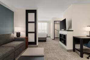 Habitación de hotel con sofá, cama, escritorio, televisión y baño visible a través de una puerta abierta.