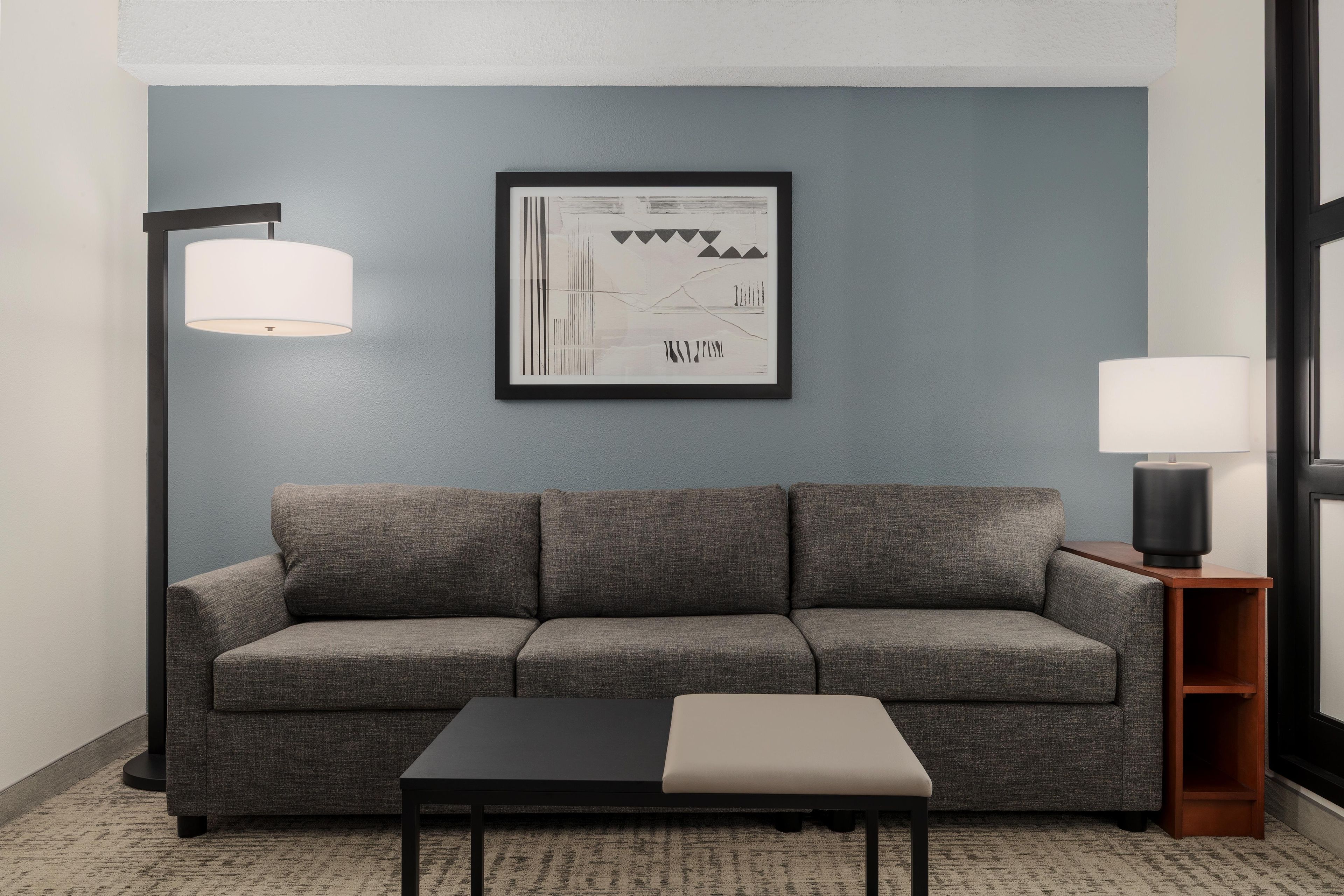 A modern living room with a grey sofa, a black coffee table, and a framed abstract artwork on the wall.