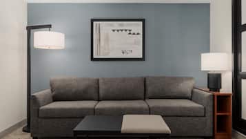 Uma sala de estar moderna com um sofá cinza, uma mesa de centro preta e uma obra de arte abstrata emoldurada na parede.