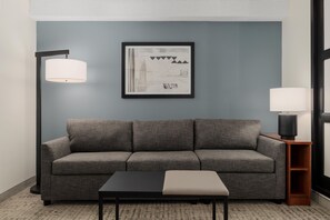Una sala de estar moderna con un sofá gris, una mesa de centro negra y una obra de arte abstracta enmarcada en la pared.