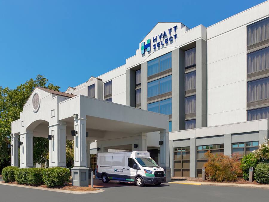 Un hotel moderno con cielo despejado, una entrada cubierta y un vehículo de servicio estacionado al frente.