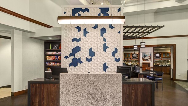 A reception area with a modern design, featuring a central counter with a marble top, a decorative wall with geometric patterns, and a wooden ceiling. - Hyatt Select Nashville/Opryland (Nashville)