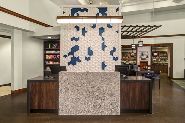 A reception area with a modern design, featuring a central counter with a marble top, a decorative wall with geometric patterns, and a wooden ceiling. - Hyatt Place Nashville Opryland (Nashville)