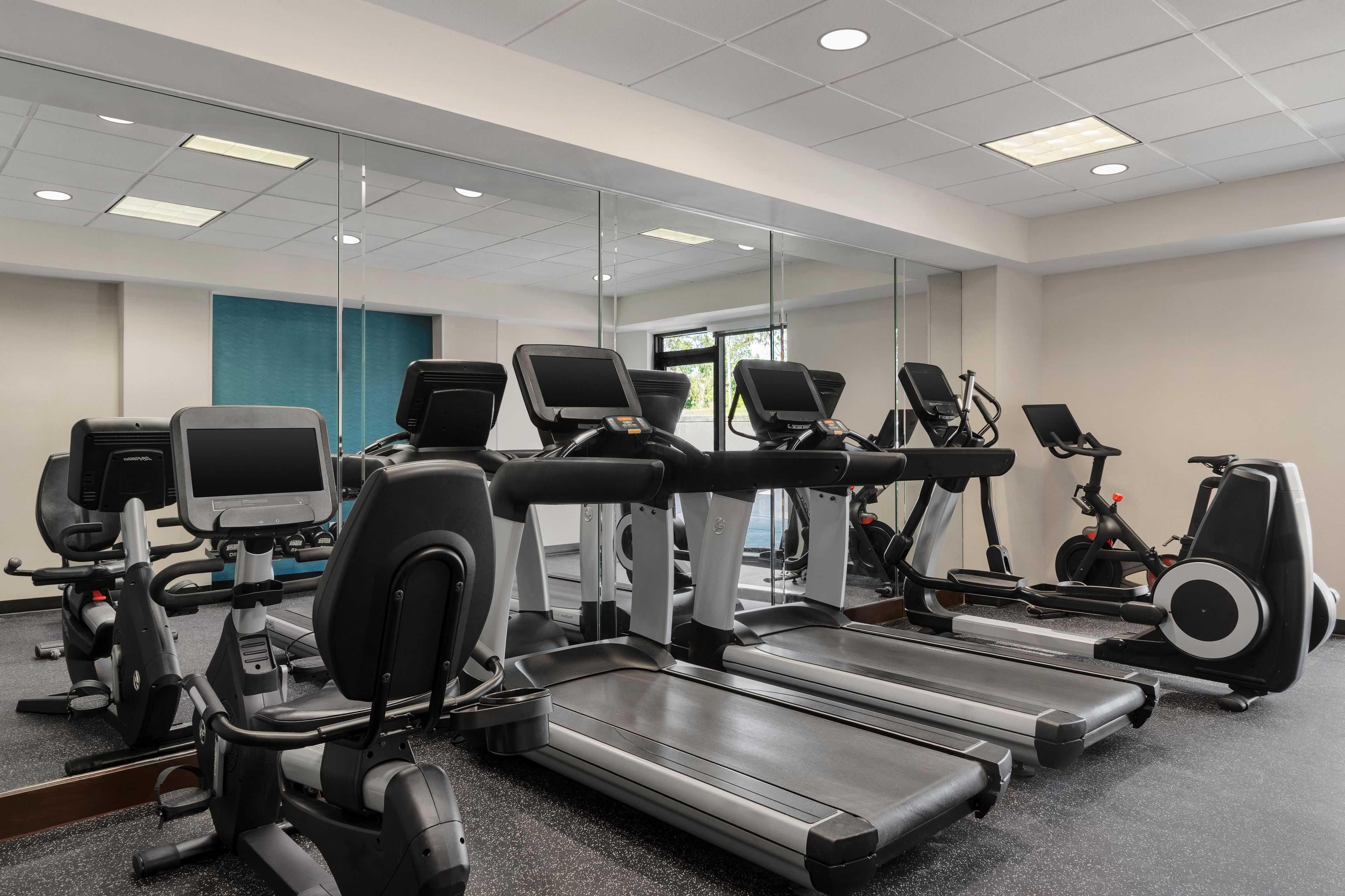 Un gimnasio con equipo de ejercicio diverso, incluyendo cintas de correr, bicicletas estáticas y máquinas elípticas.