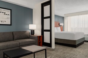 A hotel room with a sofa, a small table, a bed, and a nightstand with a lamp. - Hyatt Select Nashville/Opryland (Nashville)