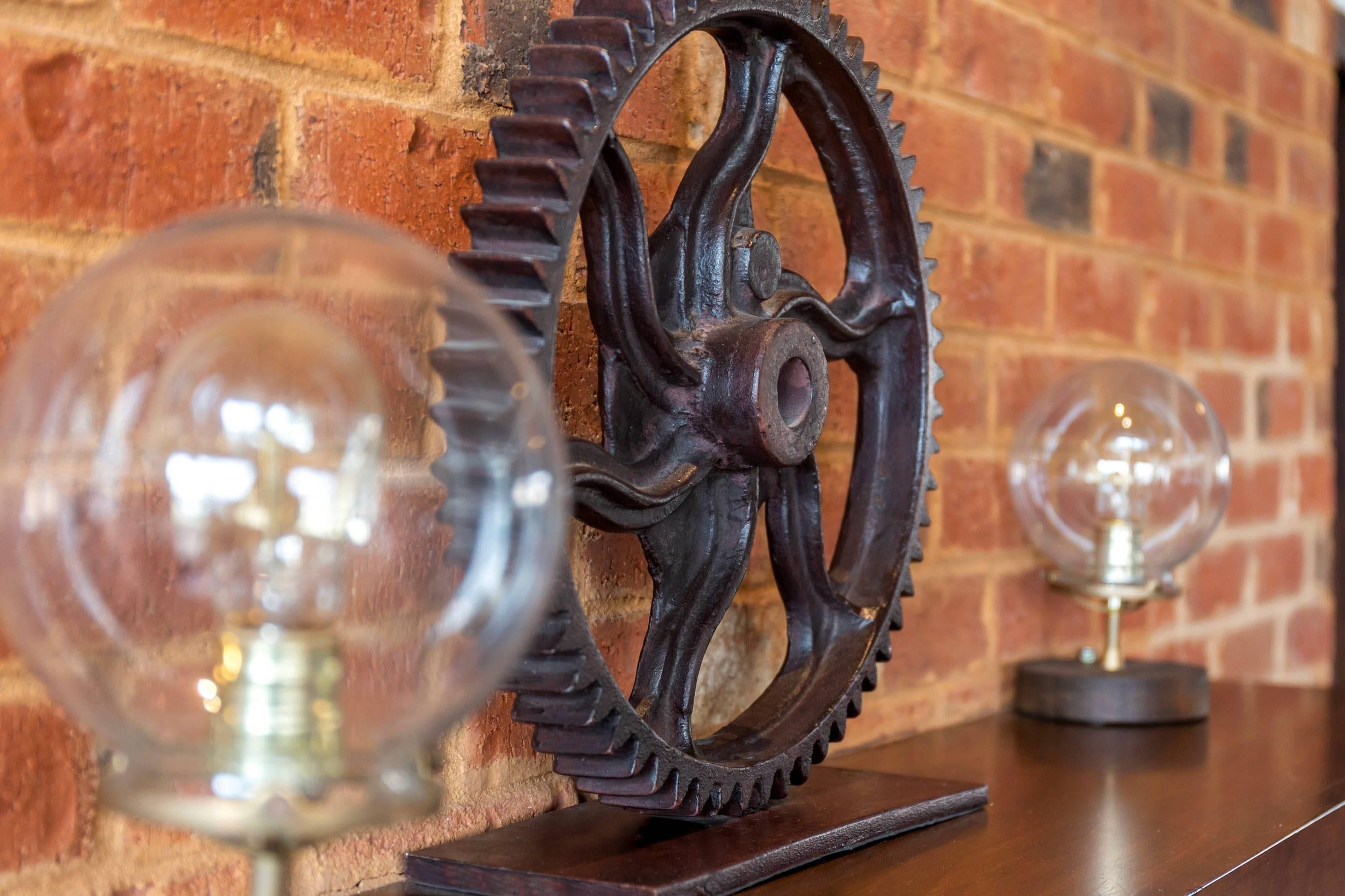 A wooden gear with a glass sphere on top, placed on a wooden surface against a brick wall.