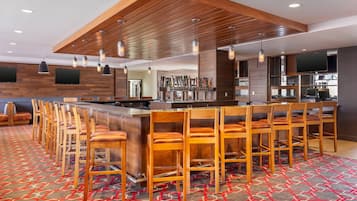 A bar area with wooden bar stools, a long counter, and a variety of bar tools.