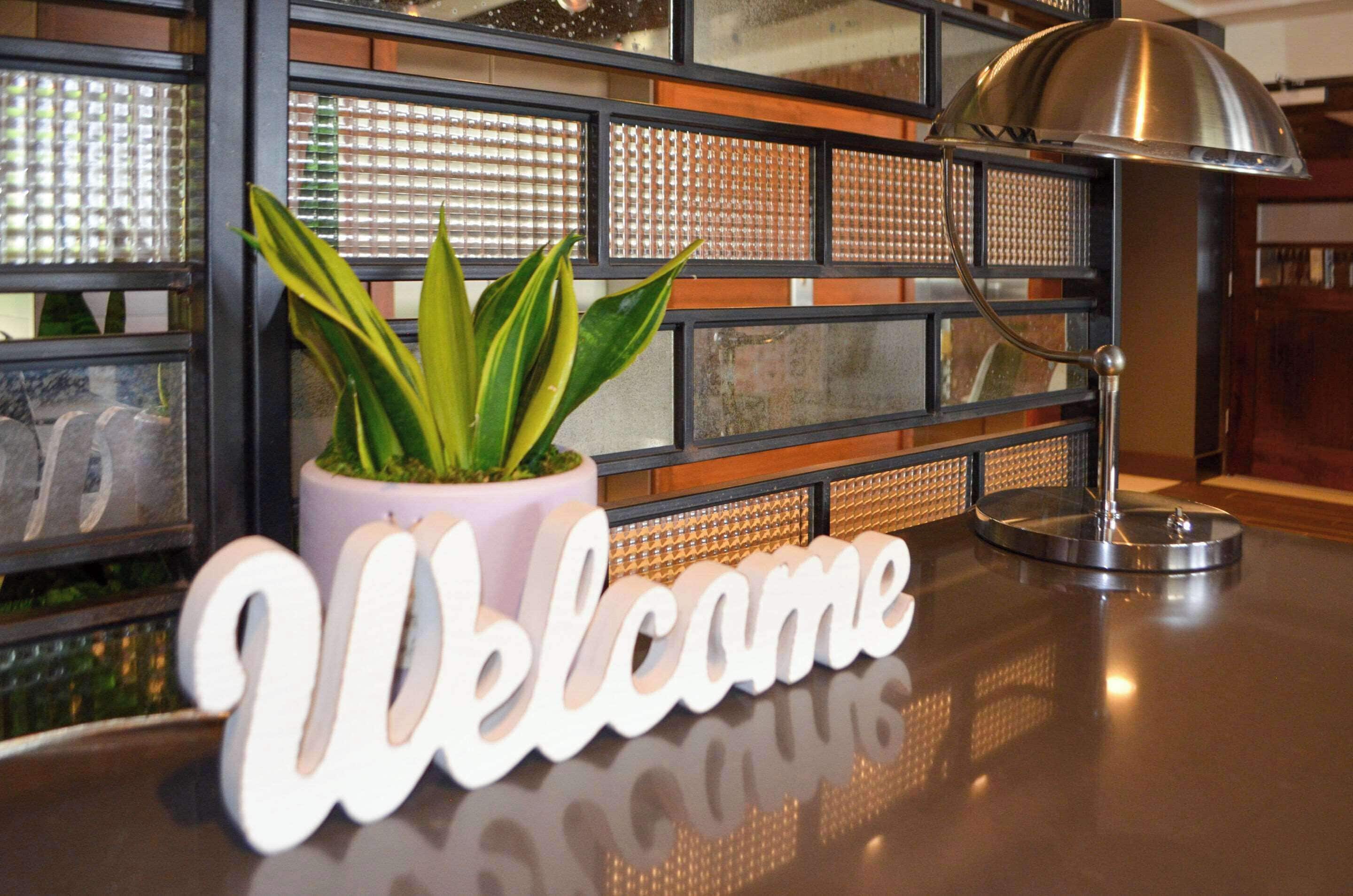 A reception desk with a 'Welcome' sign, a potted plant, and a lamp.
