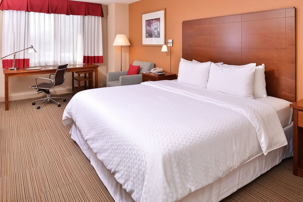 A hotel room with a large bed, a desk with a chair, a lamp, and a nightstand with a phone.