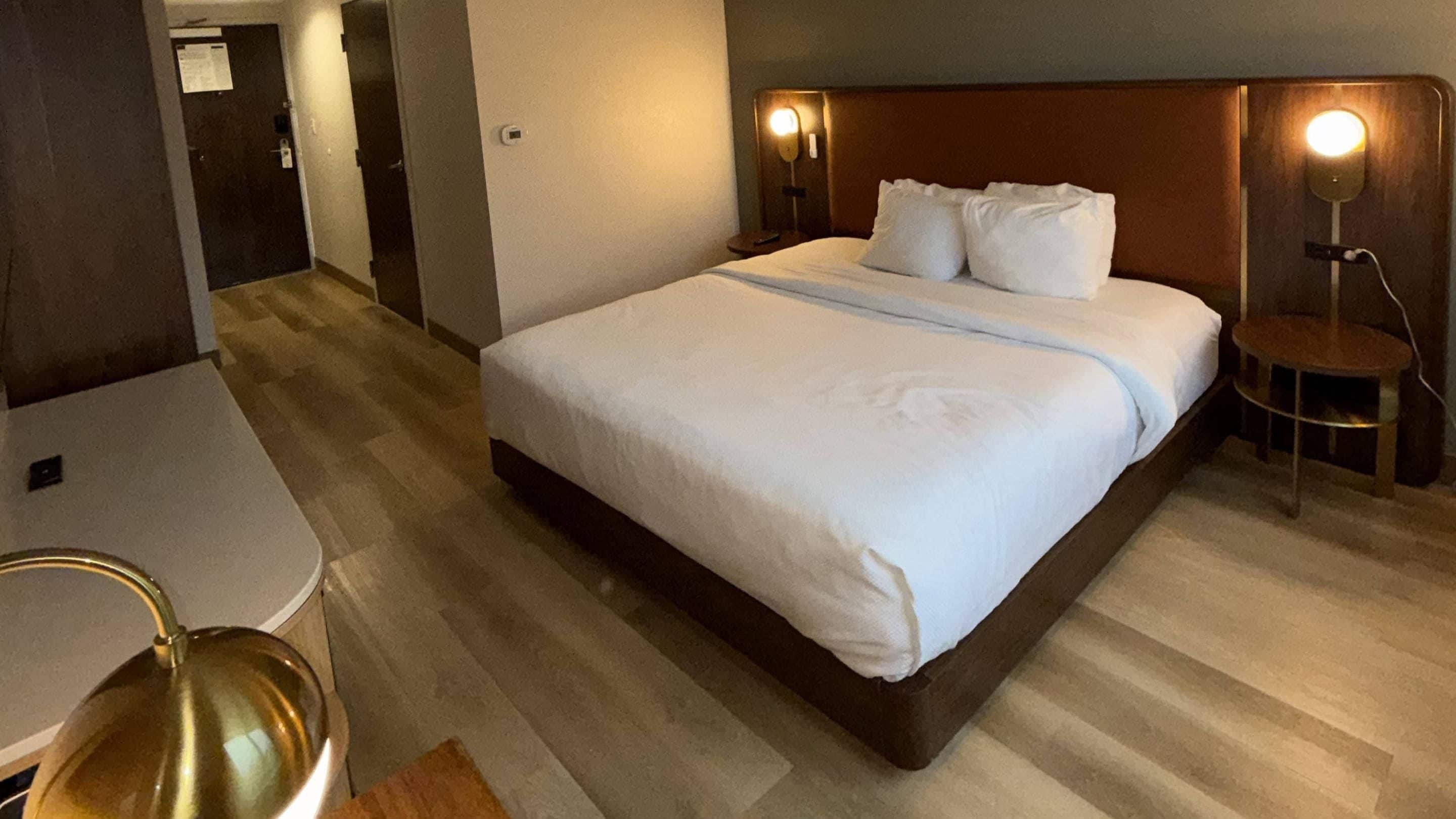 Una habitación de hotel con cama, lámparas de noche, una mesita y una silla.