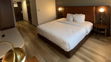 Una habitación de hotel con cama, lámparas de noche, una mesita y una silla.