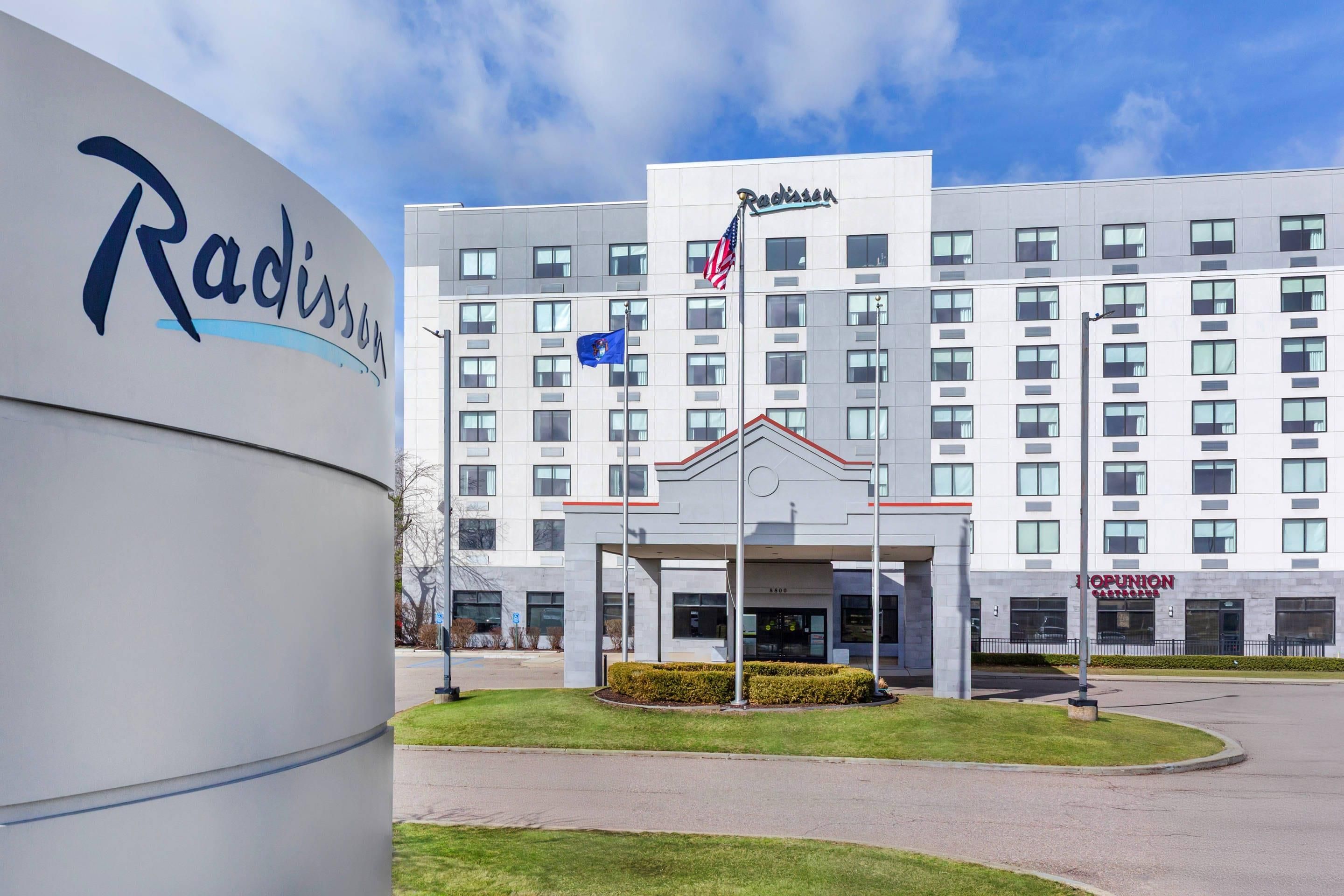 A Radisson hotel with a modern facade, a flagpole with the American flag, and a well-maintained lawn.