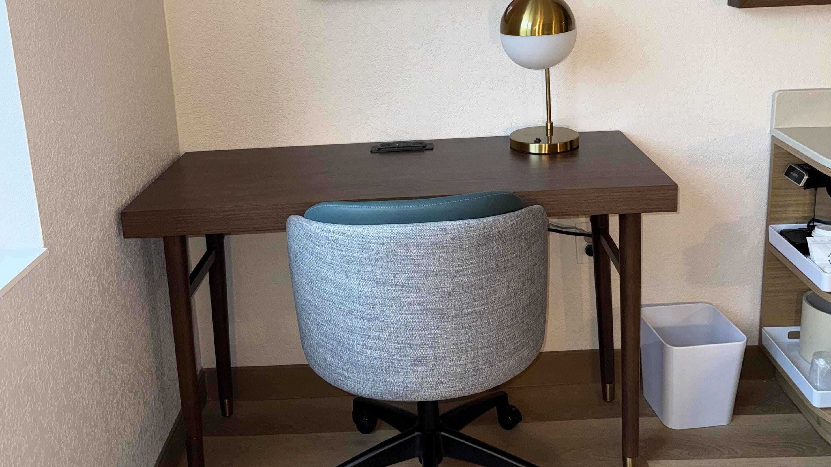 A workspace with a desk, a chair, a lamp, and a trash bin.