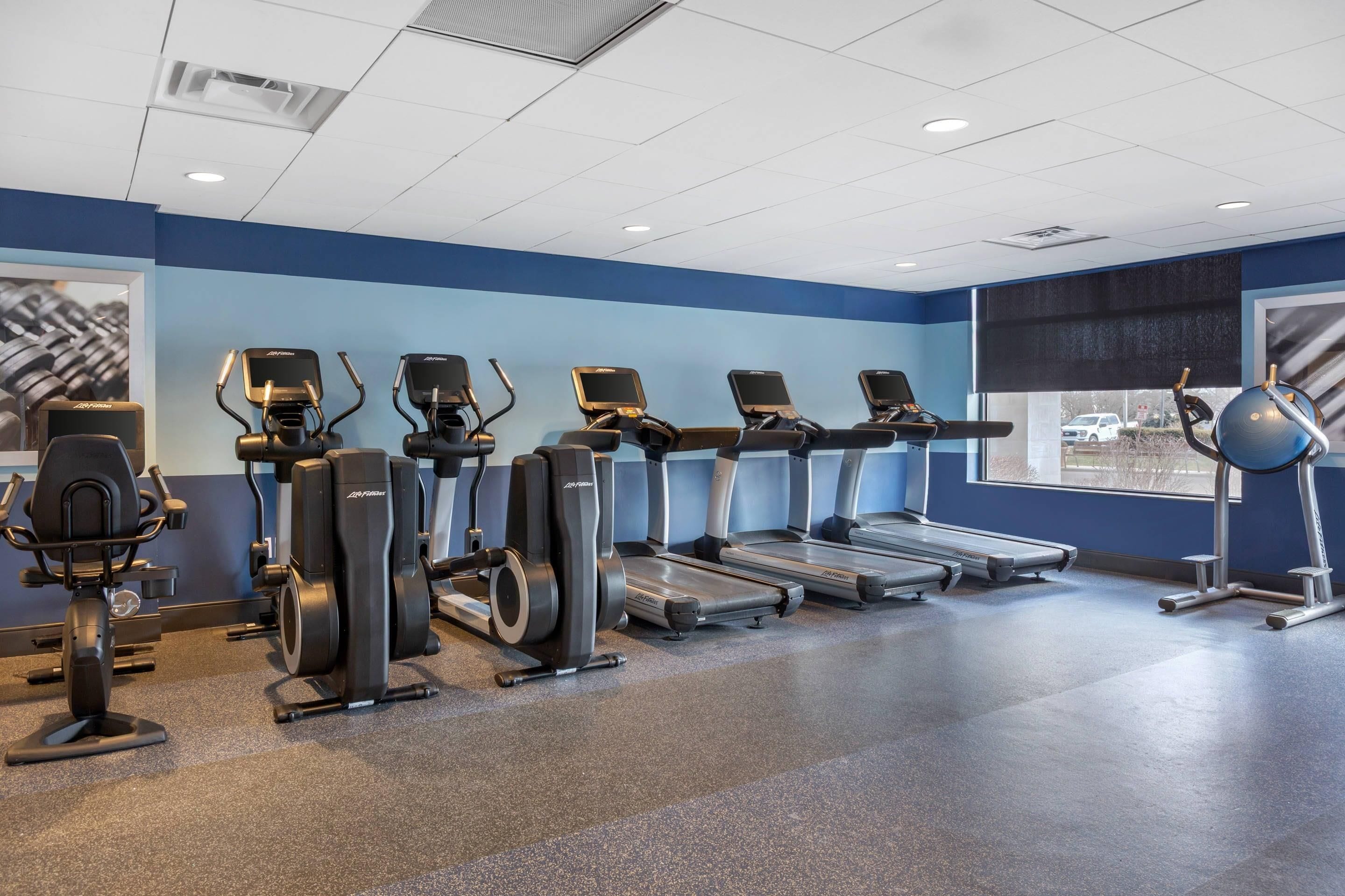 A gym with various cardio equipment including treadmills, elliptical machines, and a stationary bike.