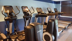A row of cardio machines including ellipticals and treadmills in a gym with blue walls and a window. - Radisson Hotel Detroit Metro Airport (Romulus)