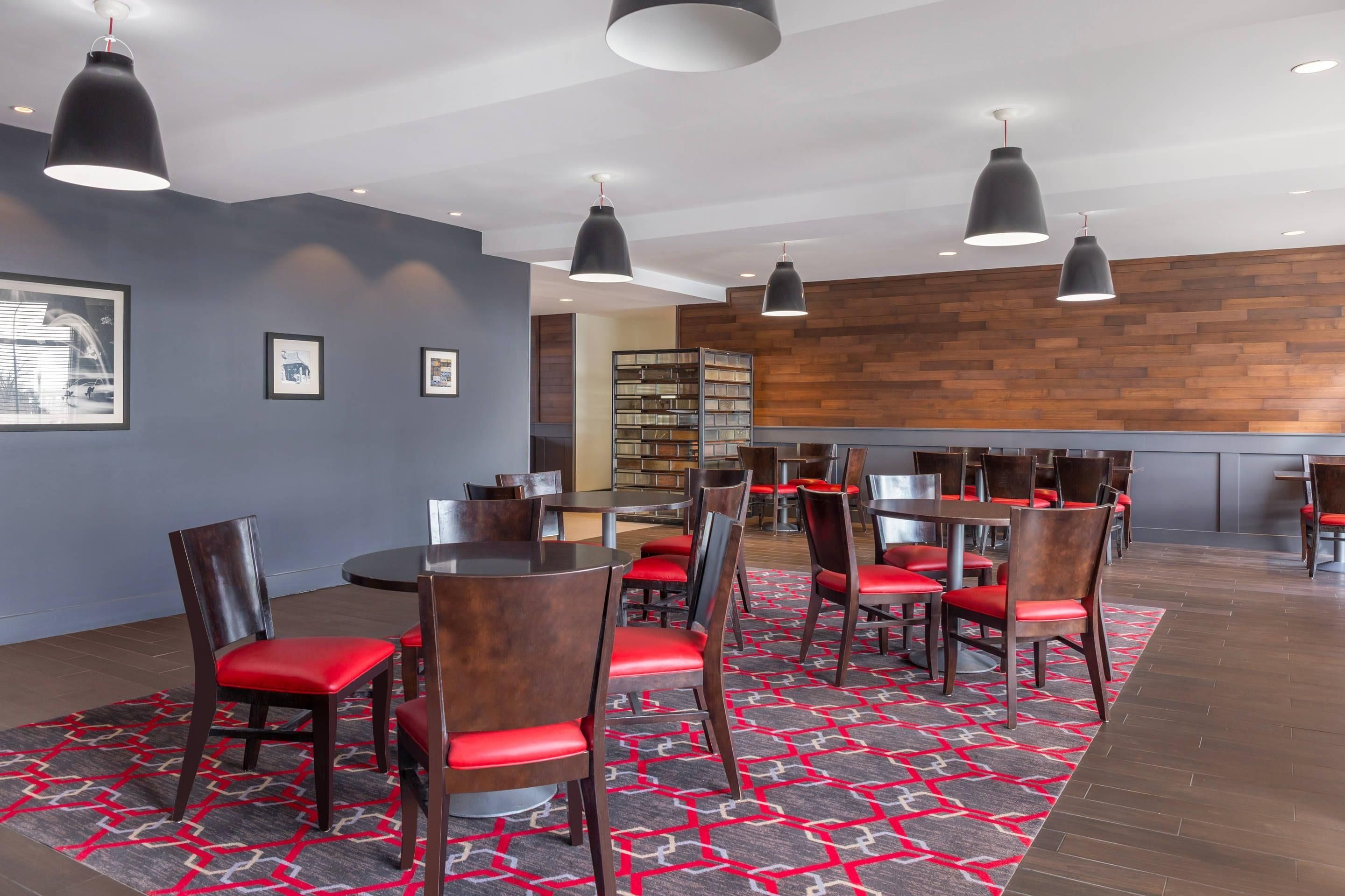 A modern dining area with round tables, red cushioned chairs, and black pendant lighting.