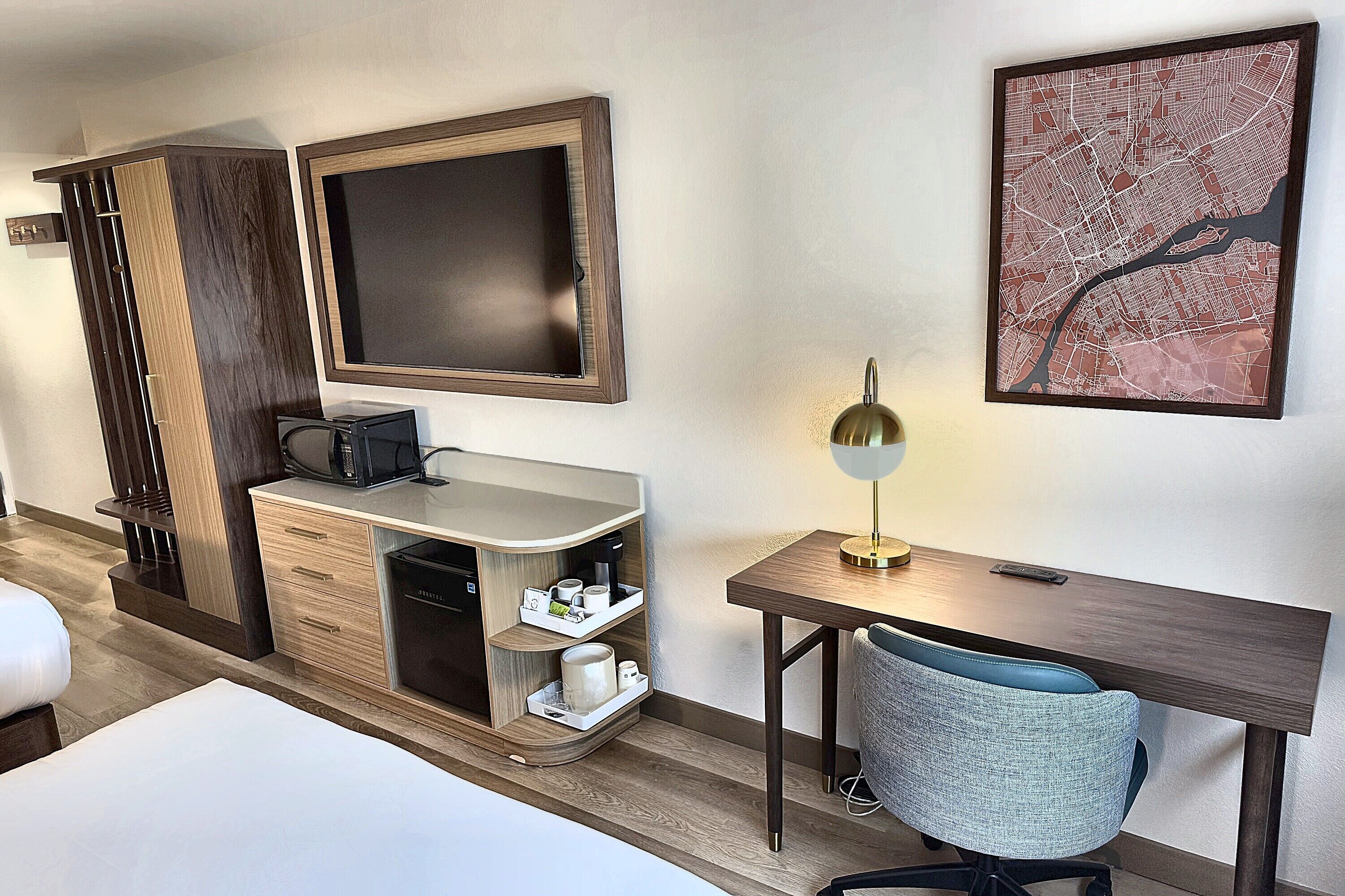 A hotel room with a bed, a desk, a chair, a coffee machine, a microwave, and a large framed map on the wall.