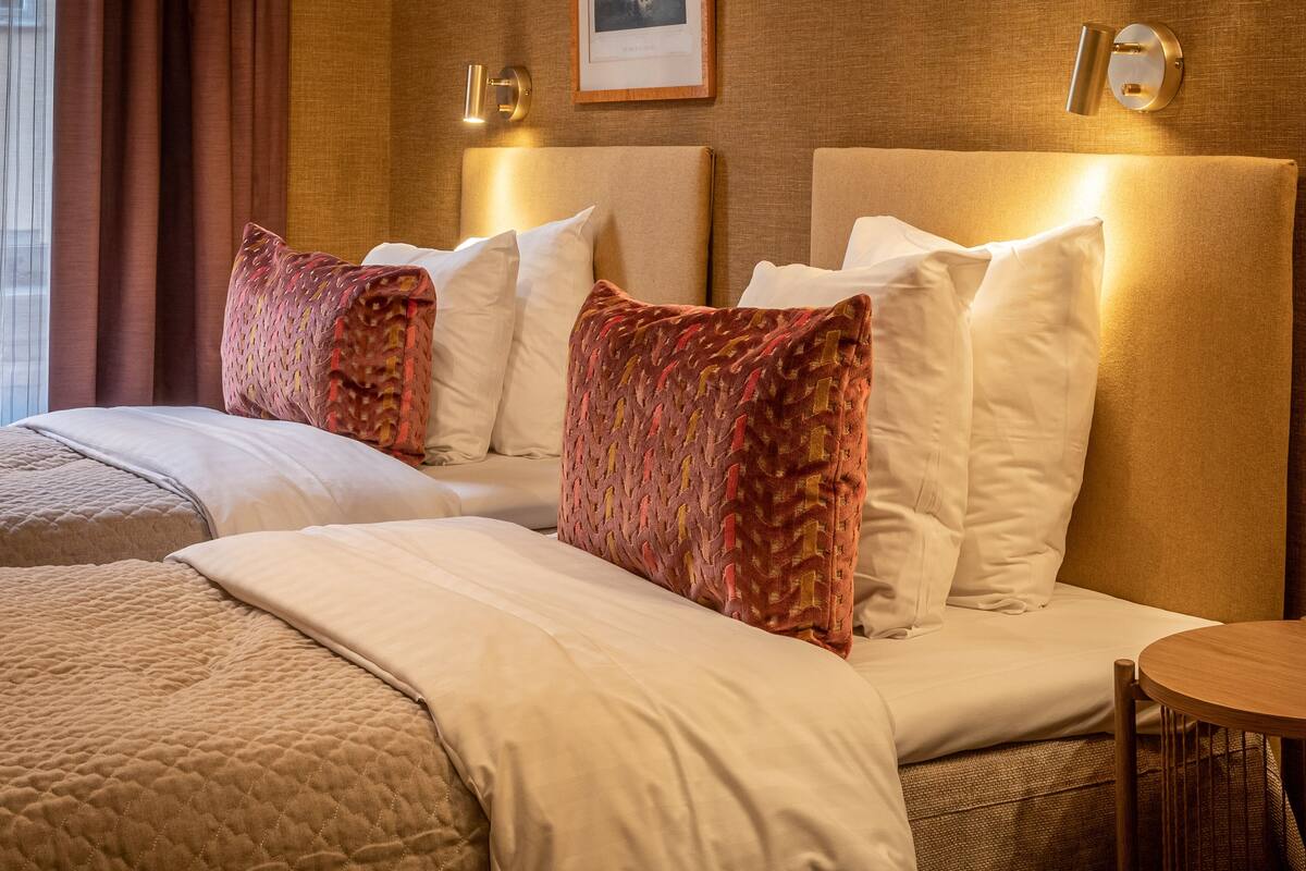 A hotel room with a large bed, multiple pillows, a bedside table, and a wall-mounted light fixture.