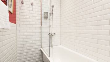 Un bagno moderno con piastrelle bianche tipo metro, una cabina doccia in vetro e una vasca da bagno bianca.
