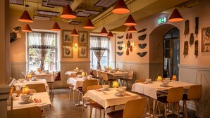 Un comedor con mesas dispuestas para el servicio, iluminación colgante y obras de arte en las paredes.