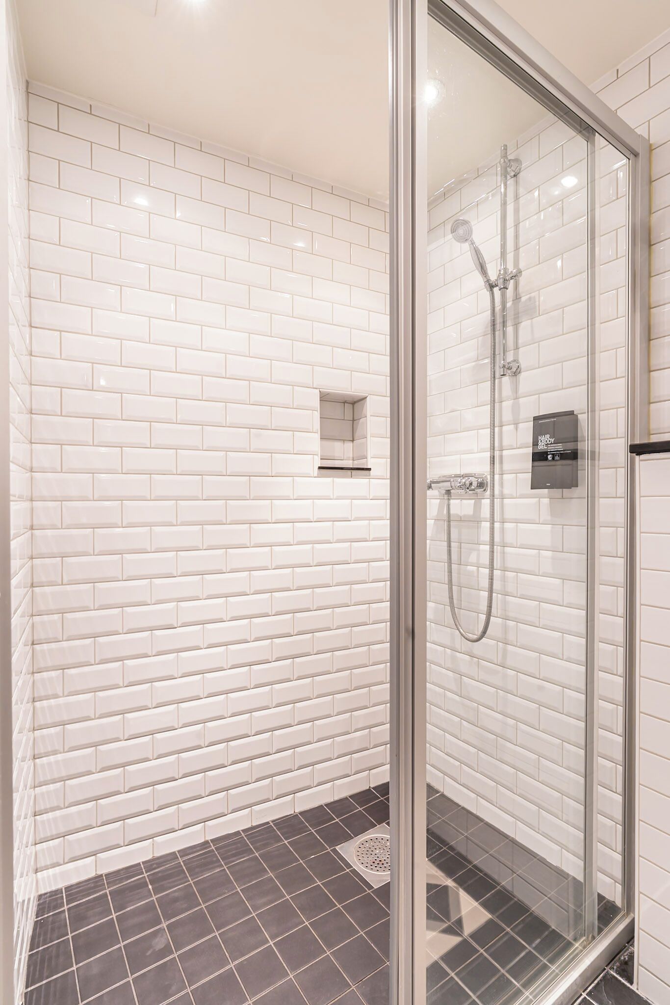 A modern bathroom with white subway tile walls, a glass shower enclosure, and a dark tiled floor.