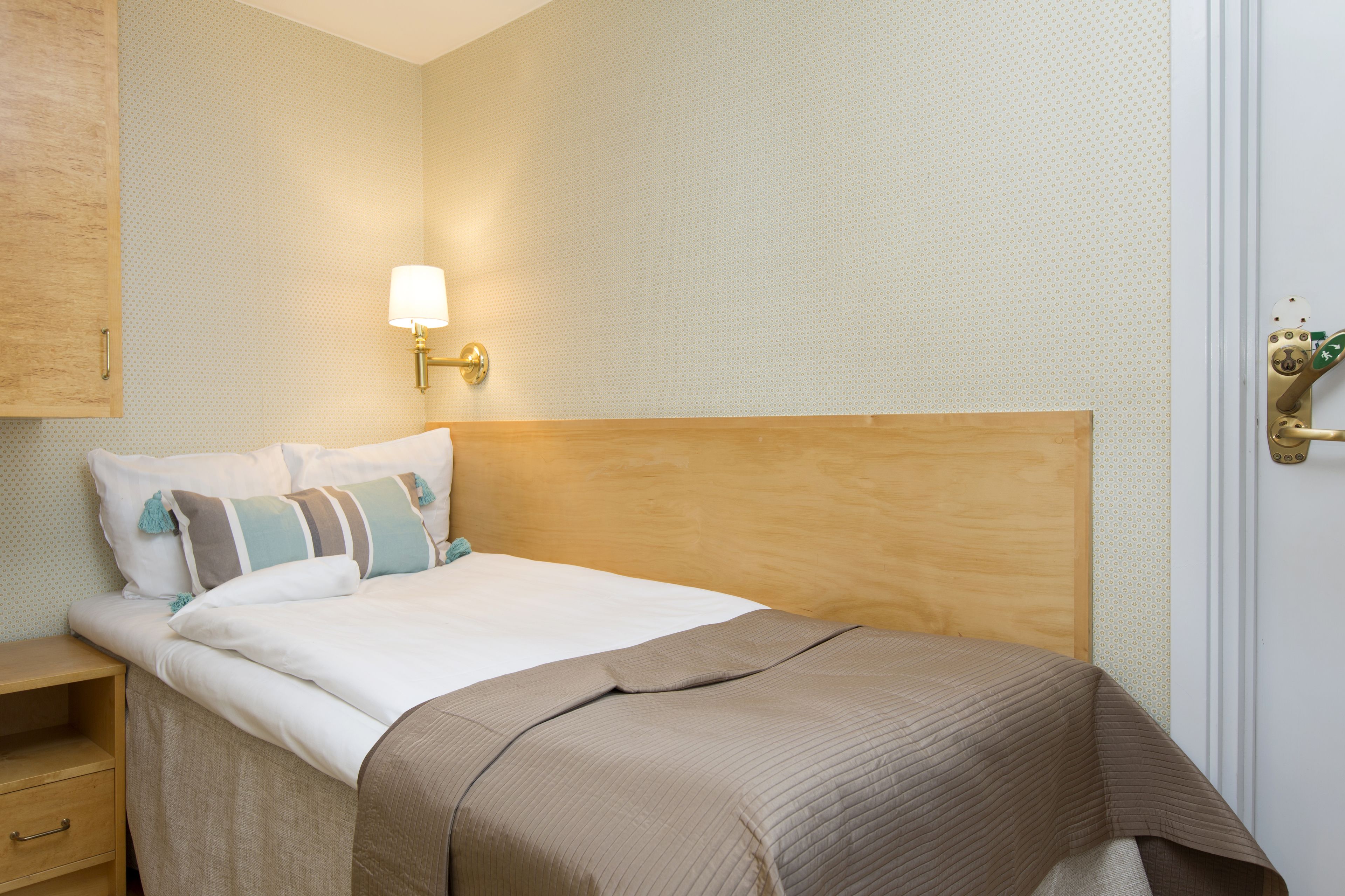 A neatly made bed with a wooden headboard, a bedside table with a drawer, and a wall-mounted lamp.