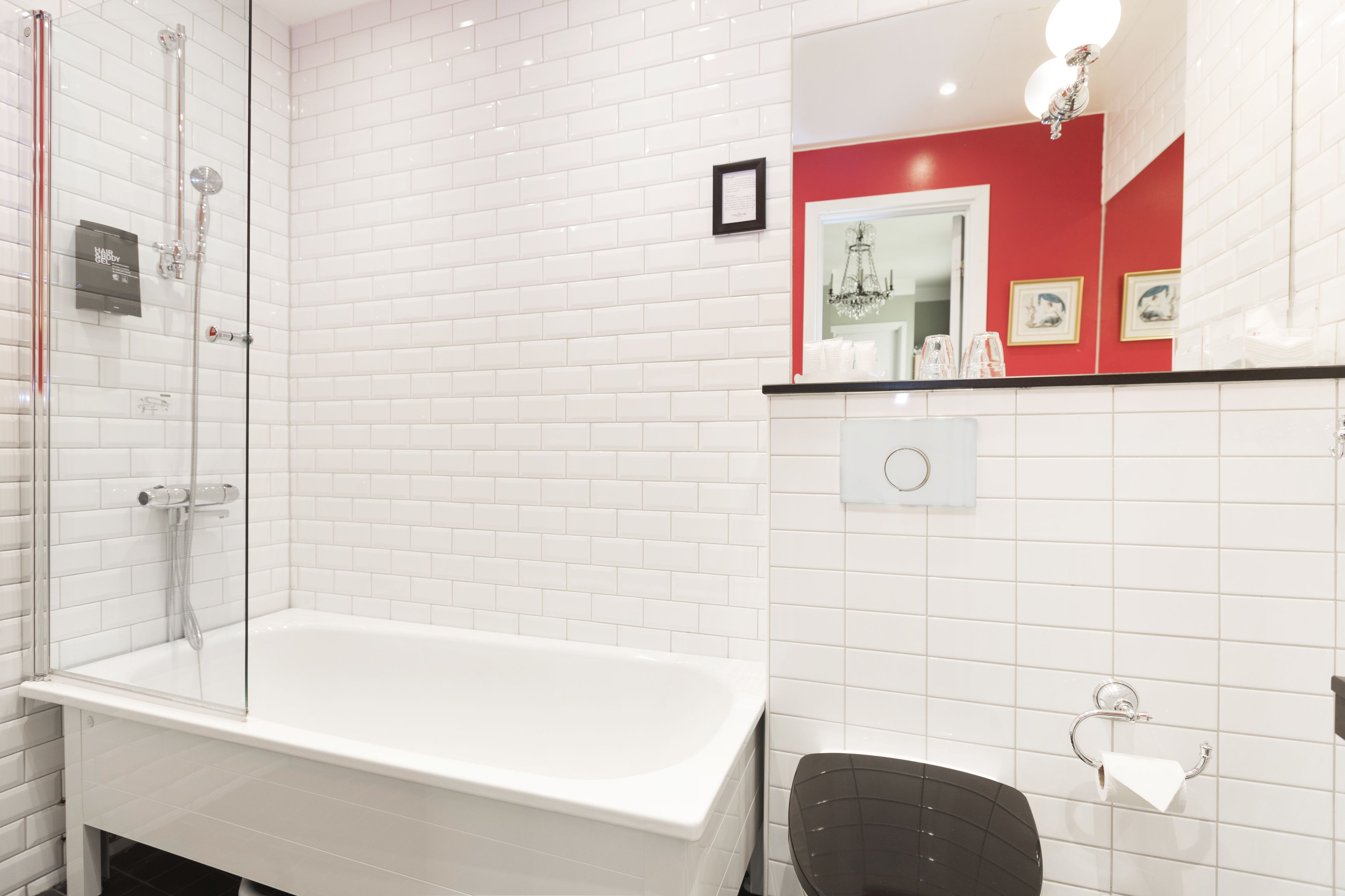 A bathroom with a white bathtub, a glass shower enclosure, a black toilet, and a red accent wall.
