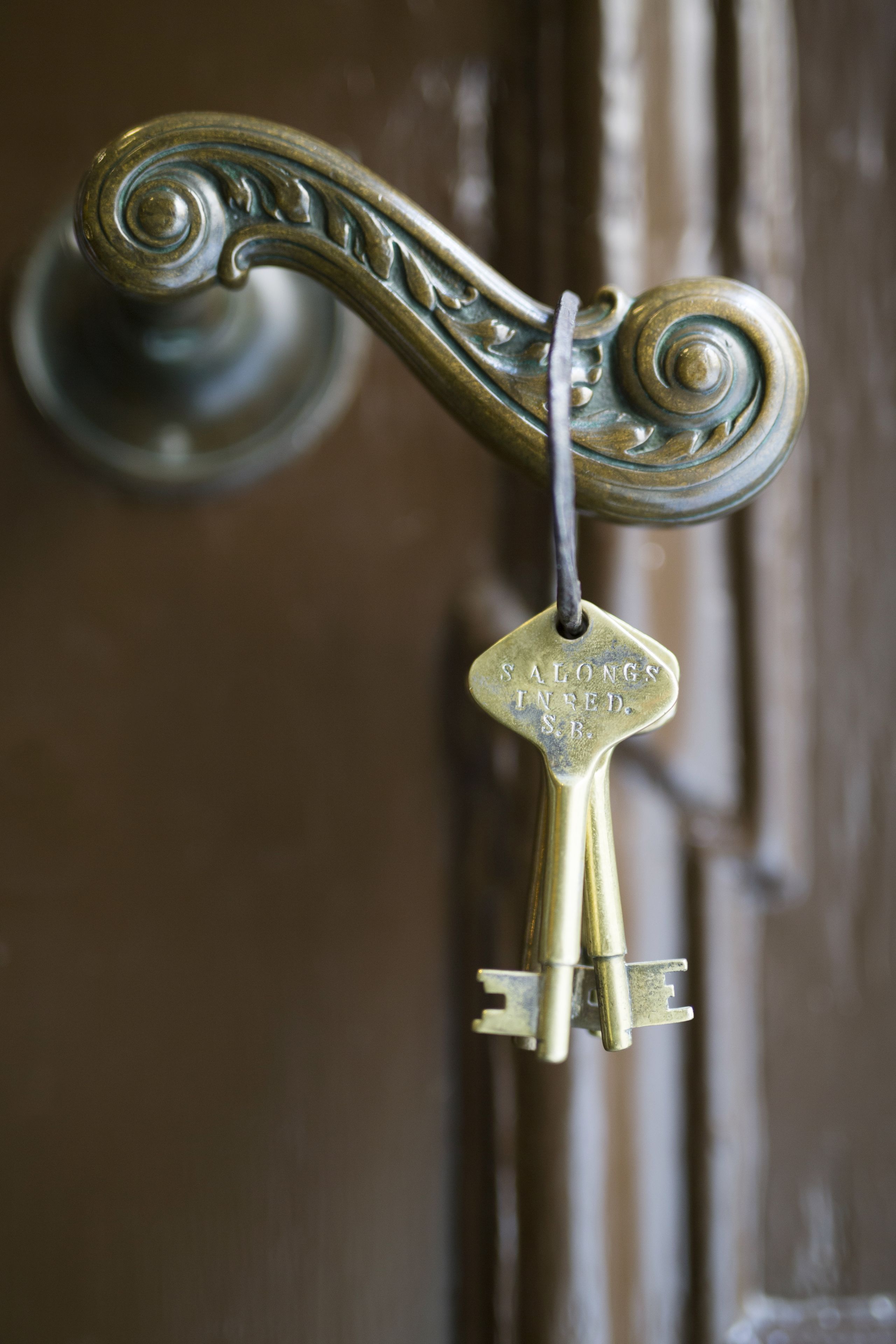 A brass key with the inscription "S. ALONGS IN BED. S.B." hanging on a door handle.