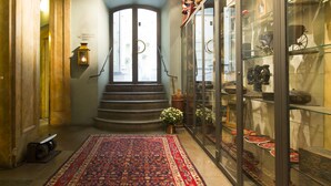 Un pasillo con alfombra roja estampada, un expositor de vidrio con varios objetos, y una escalera que lleva a una puerta con panel de vidrio esmerilado.
