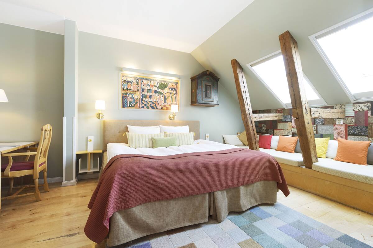 A bedroom with a bed, a desk, a chair, a window, and a painting on the wall.