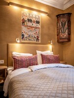 Una cama bien hecha con almohadones estampados, un tapiz colgado en la pared y un aparador de madera.