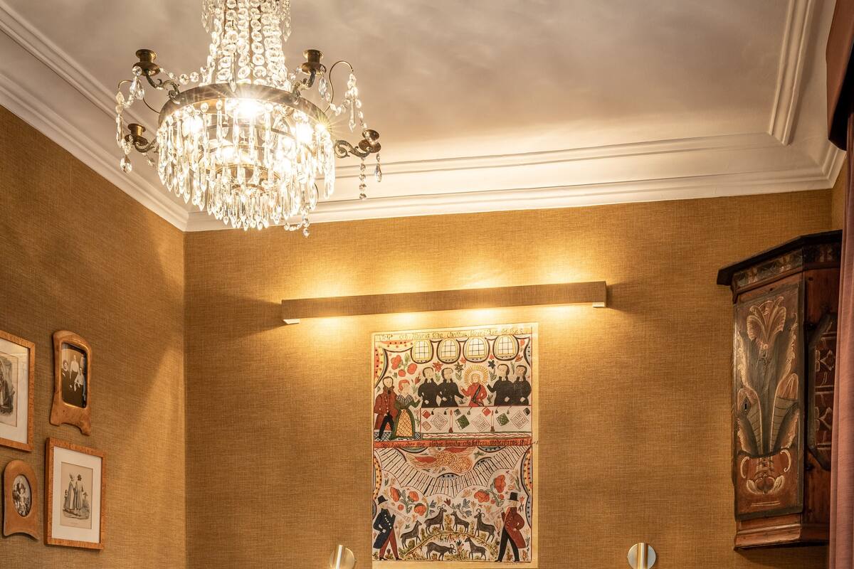 A hotel room with a large bed, a chandelier, a wall-mounted artwork, and a wooden cabinet.