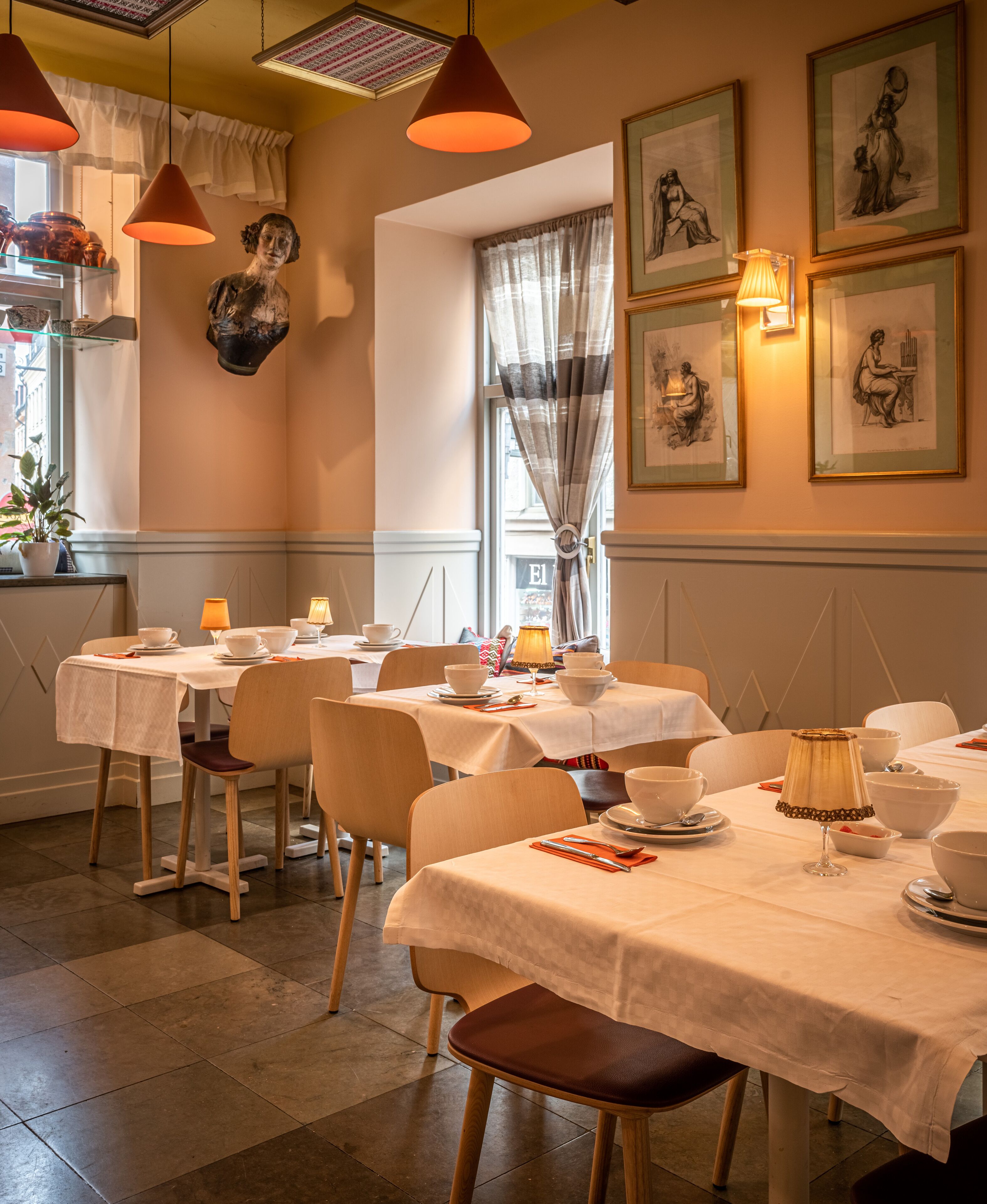 Un espace repas avec des tables dressées, une fenêtre avec des rideaux et des œuvres d’art accrochées au mur.