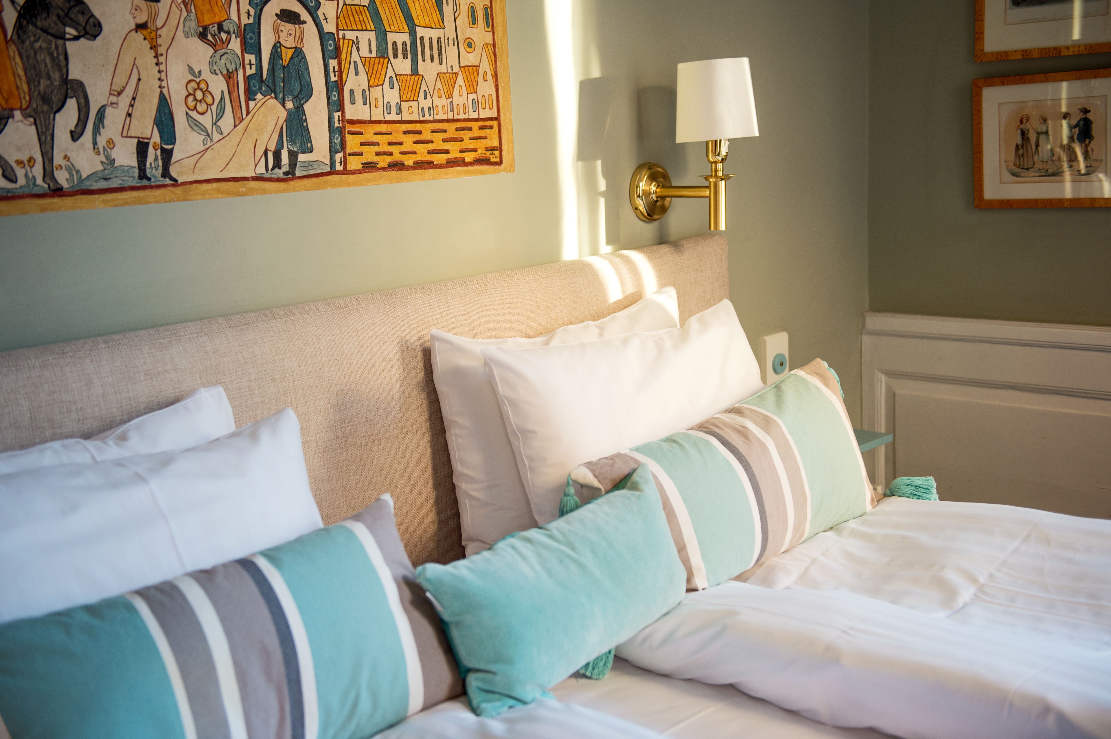 A neatly made bed with striped pillows, a wall-mounted lamp, and a framed picture above it.