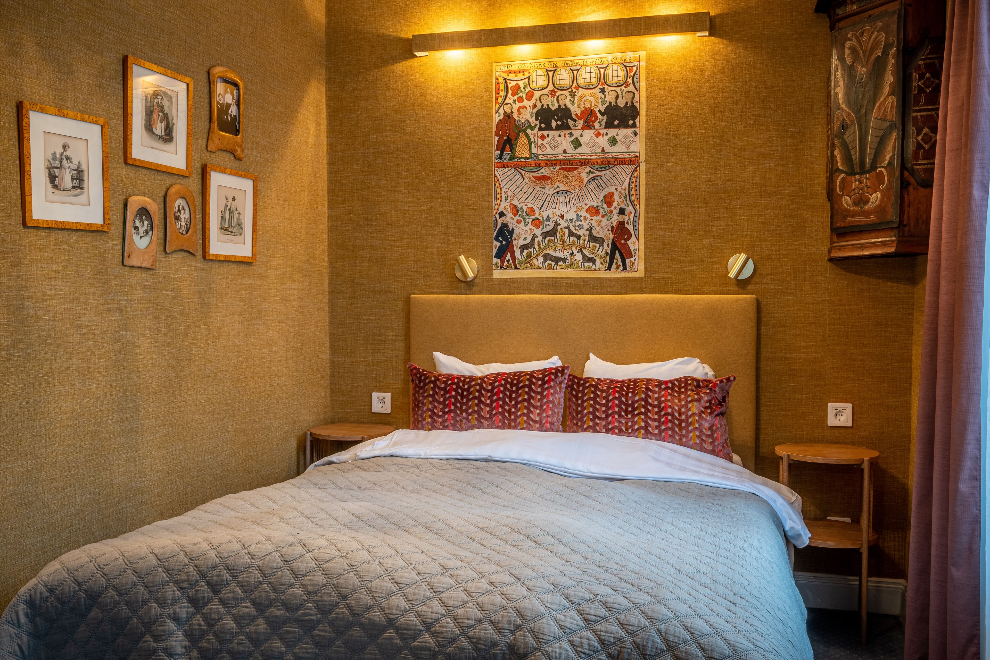 A hotel room with a large bed, a headboard with a decorative panel, a wall-mounted artwork, and a small wooden nightstand.