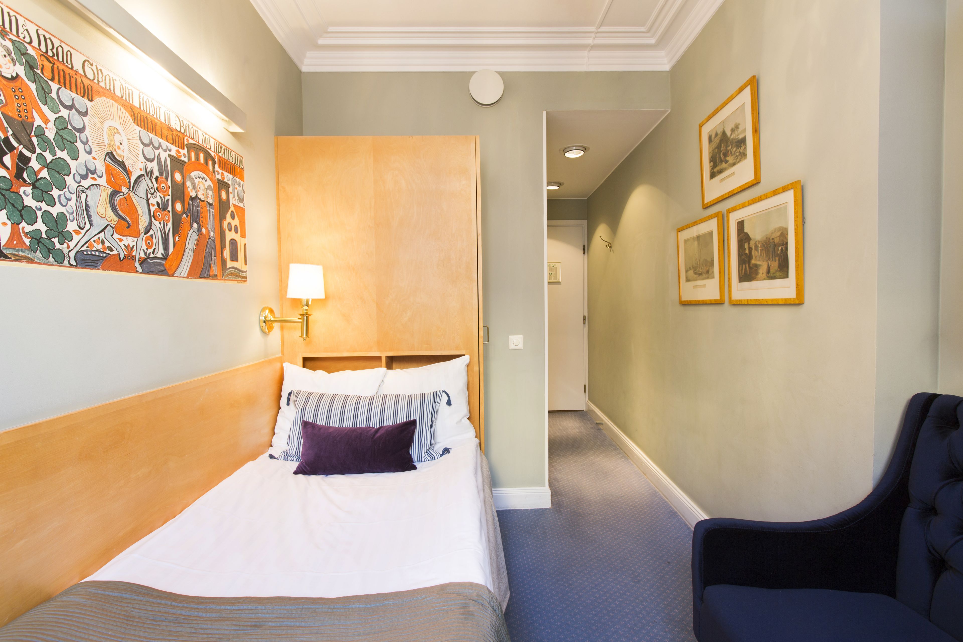 A hotel room with a bed, a chair, a wall with a mural, and framed pictures on the wall.