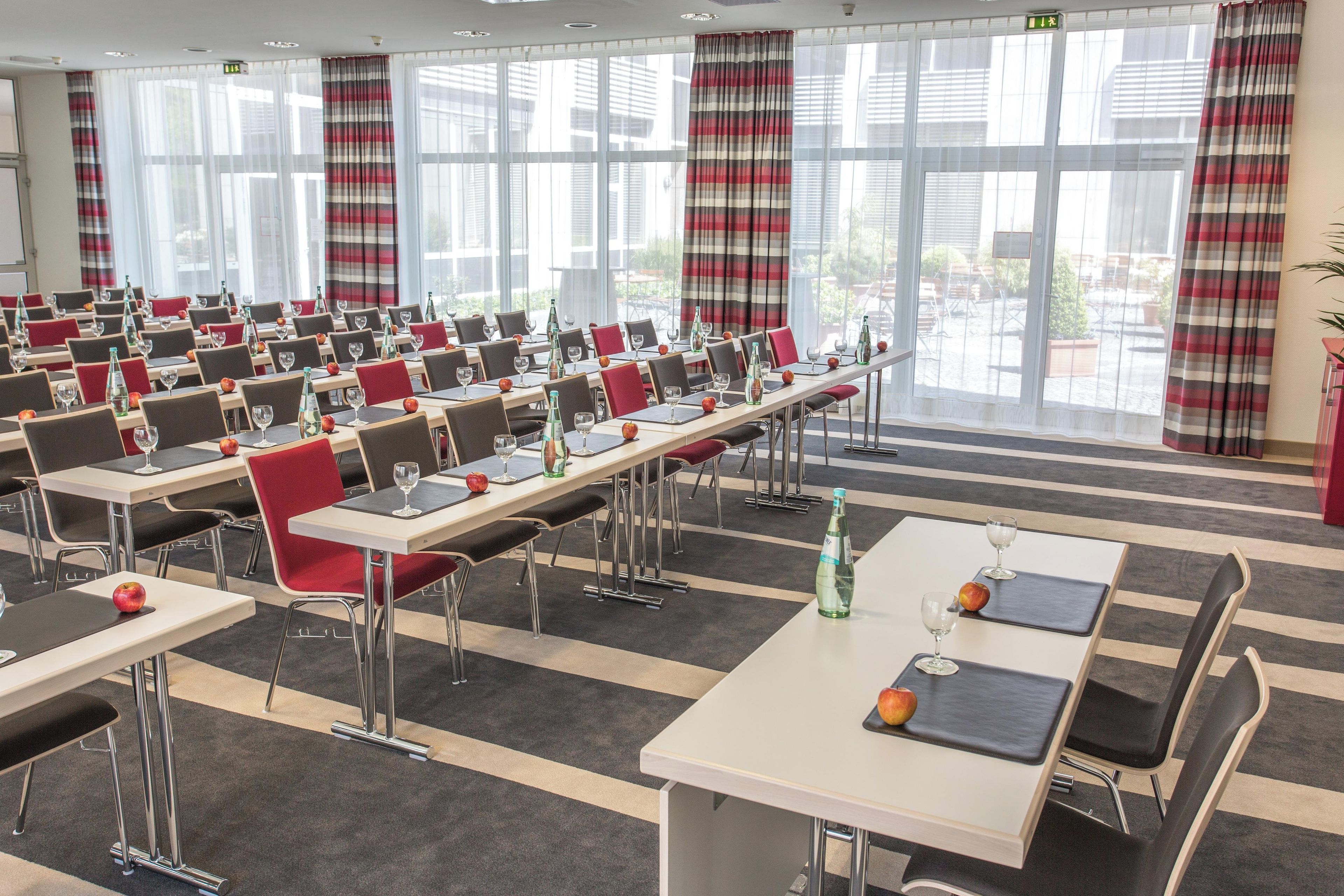 A conference room with tables, chairs, and a large window with curtains.