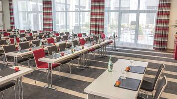 A conference room with tables, chairs, and a large window with curtains.