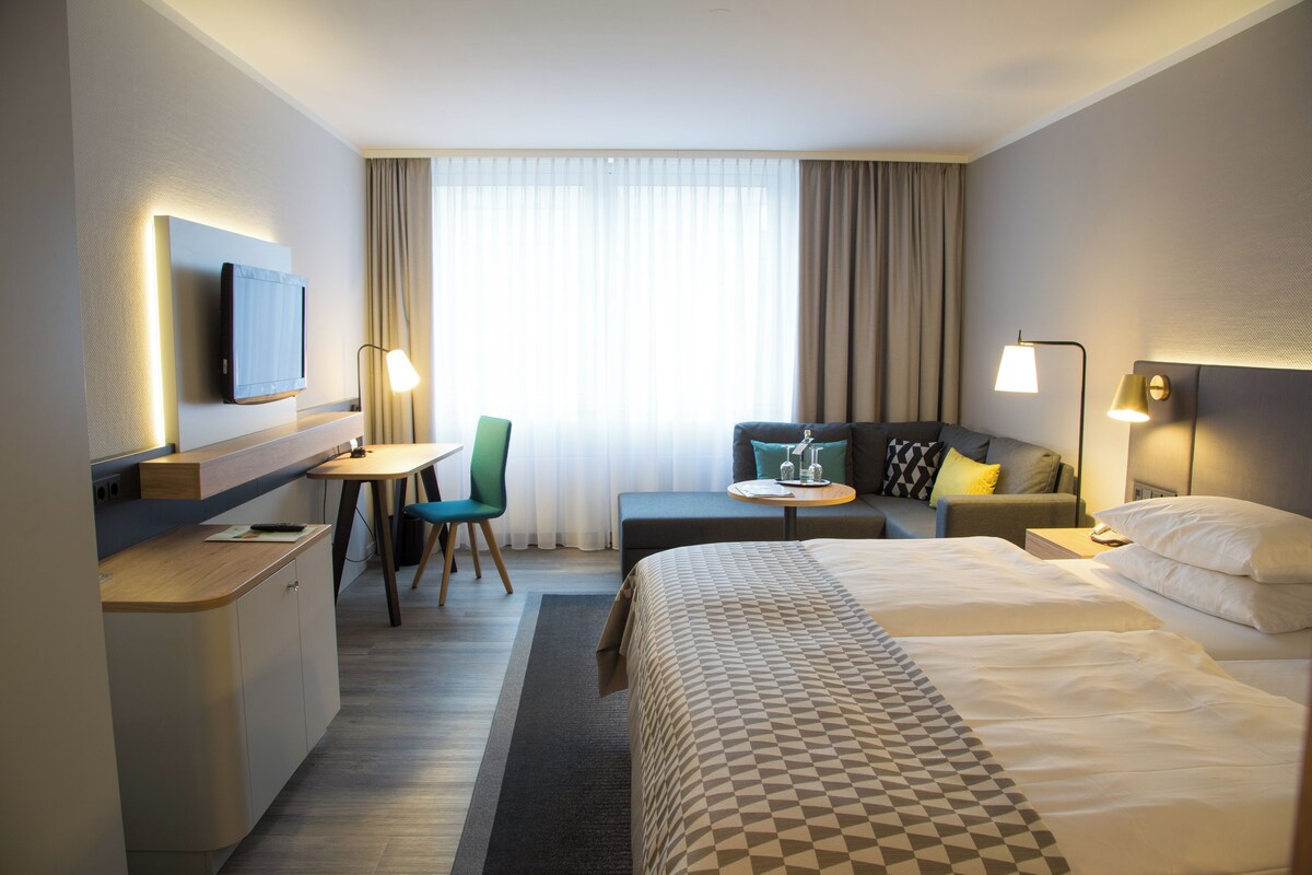 Une chambre d’hôtel comprenant un lit, un bureau, une chaise, un canapé et un téléviseur.