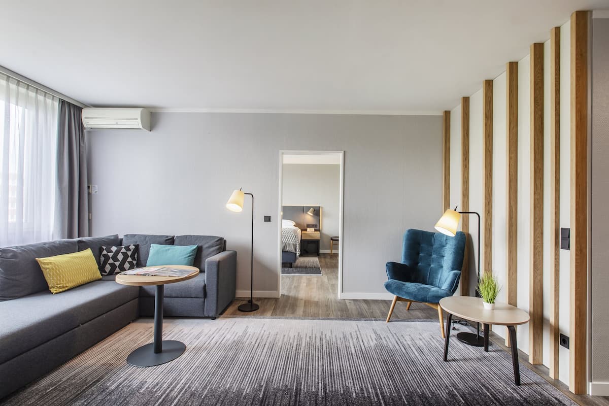 A modern hotel room with a grey sofa, a round table, a blue armchair, and a wooden partition.