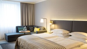 A hotel room with a large bed, a sofa, a bedside table, and a lamp. - Holiday Inn Düsseldorf - Neuss by IHG (Neuss)