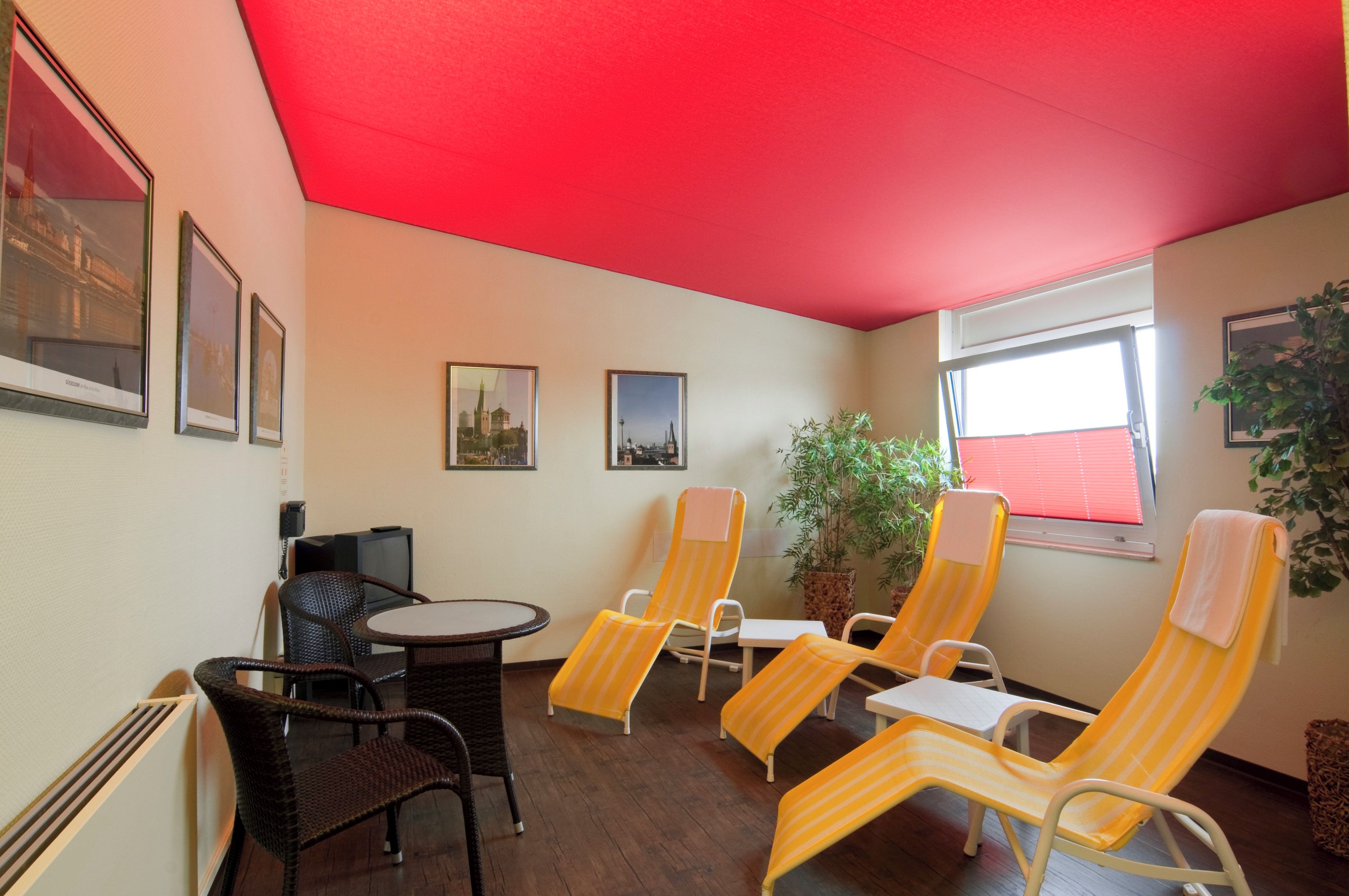A room with a red ceiling, a round table, wicker chairs, and a potted plant.