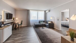 A modern hotel room with a dining area, a sofa, a bed, and a large window with curtains. - Holiday Inn Düsseldorf - Neuss by IHG (Neuss)