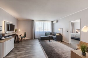 A modern hotel room with a dining area, a sofa, a bed, and a large window with curtains.
