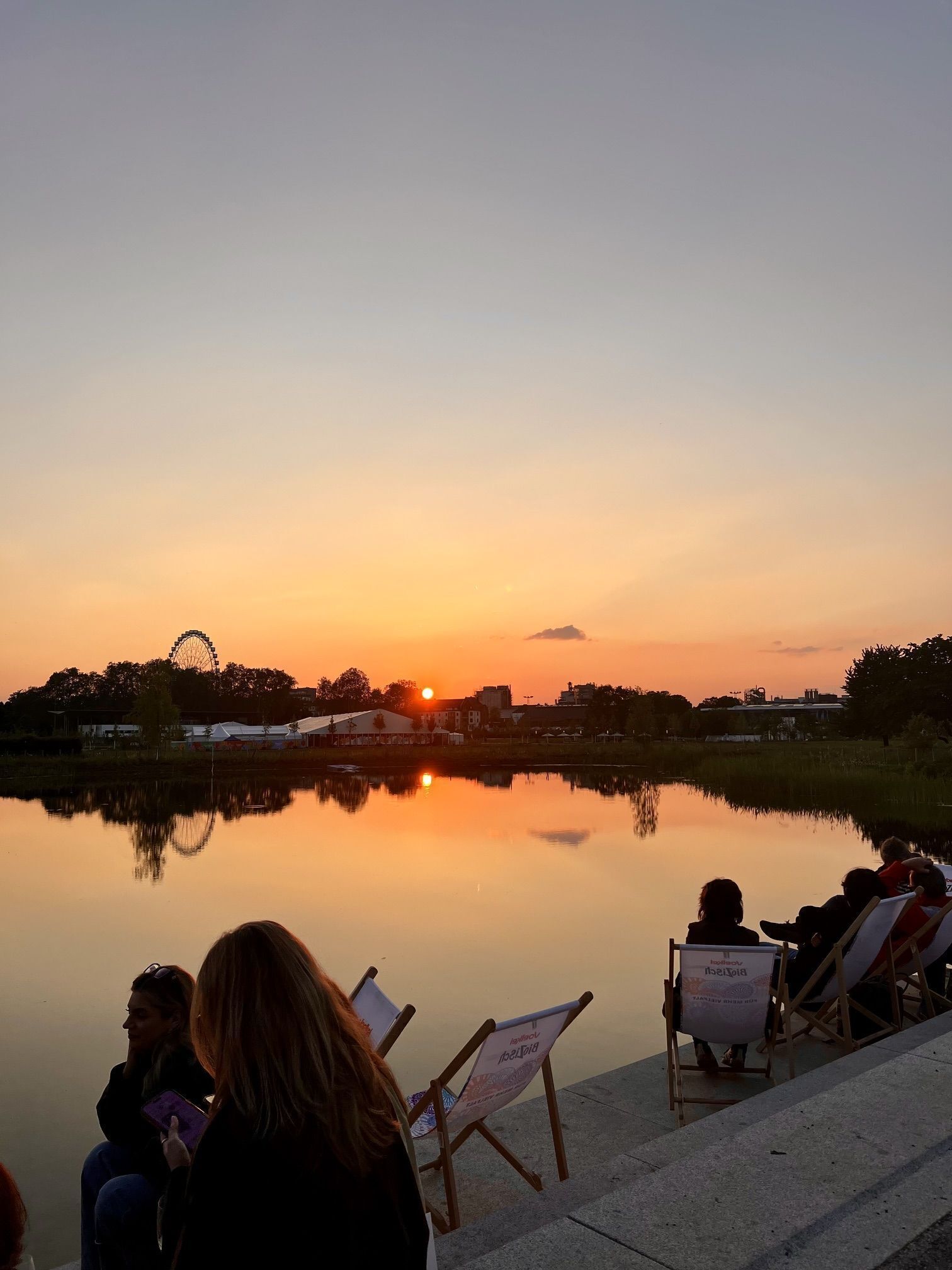 A sunset view over a calm body of water with a Ferris wheel in the background.
