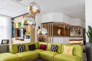 Un área de estar moderna con un sofá seccional verde, un mostrador de recepción de madera y un espejo grande.