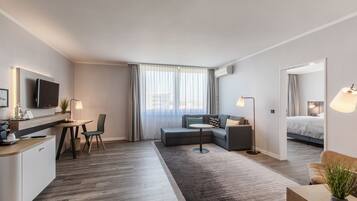 A modern hotel room with a dining area, a sofa, a bed, and a large window with curtains.