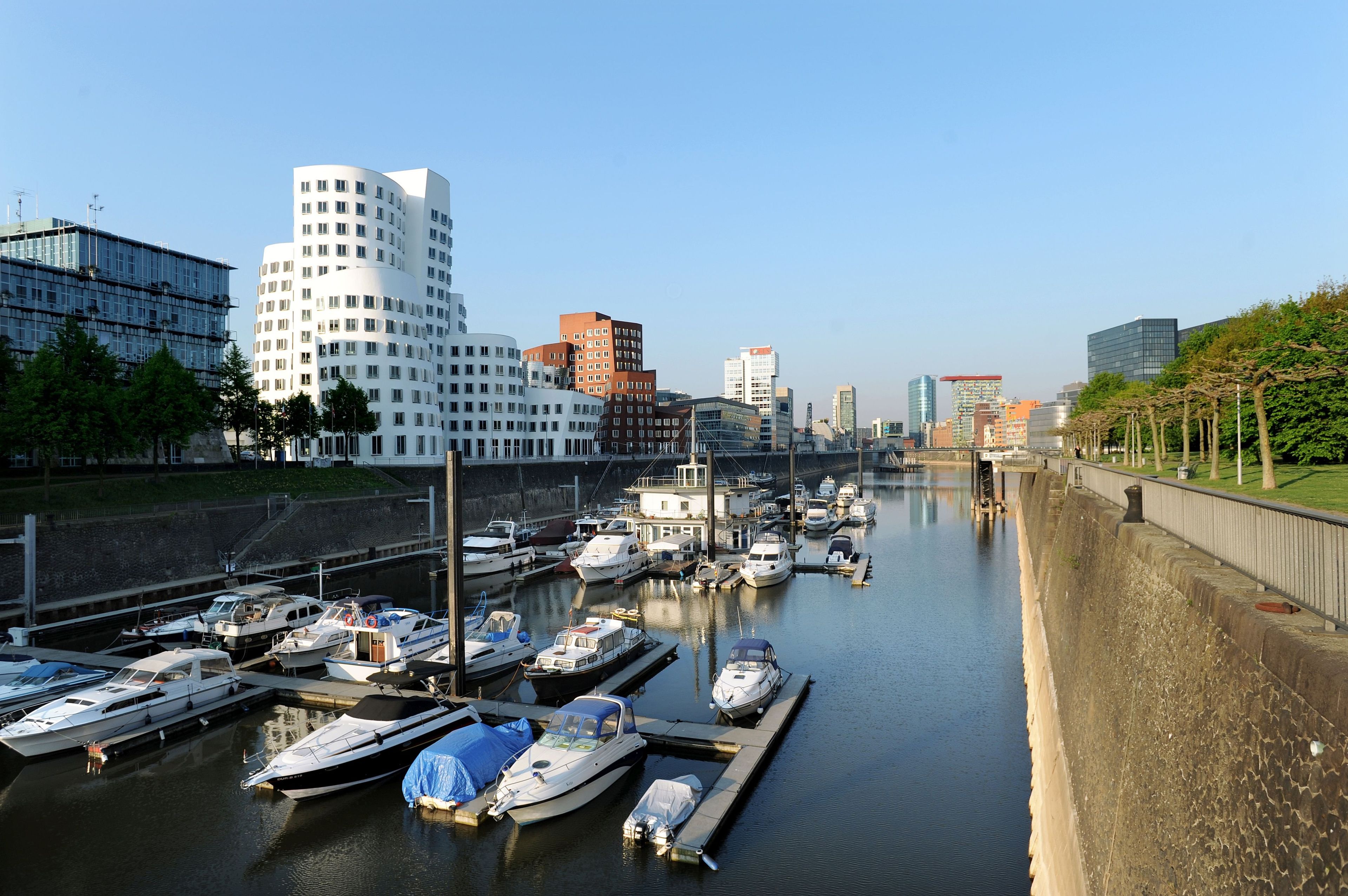 A marina with boats docked, surrounded by modern buildings and a clear sky.